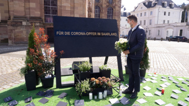Pressefoto: Oberbürgermeister Uwe Conradt legt einen Blumenstrauß zum Gedenken an die Corona-Opfer im Saarland vor der Ludwigskirche nieder. (Quelle: LHS) Image