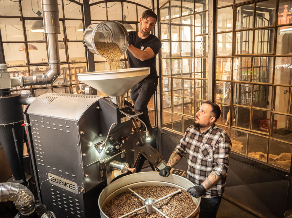 Kai Adam und Kolja Conrad beim Befüllen der Röstmaschine mit frischen Bohnen Blick auf Produktion Rösterei