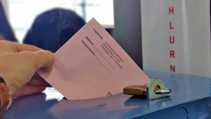 Eine Hand wirft einen Wahlumschlag in eine Urne
