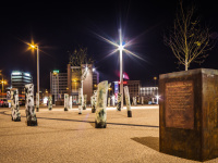 Das Mahnmal "Der Unterbrochene Wald" von Ariel Auslender auf dem Rabbiner Rülf Platz: Die Skulptur aus 40 bronzenen Baumstämmen gruppiert sich seit 2013 ungeordnet auf dem Platz und ragt ein Stück in die Freitreppe der Berliner Promenade hinein. Rabbiner-Rülf-Platz bei Nacht