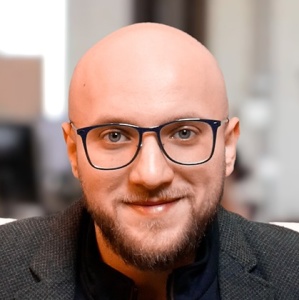 Anas Alakkad - Gründer und Geschäftsführer von Pontem Pro / Portraitfoto Portrait / Frontalaufnahme des Geschäftsführers Anas Alakkad mit Brille und Businessdress, lächelnd