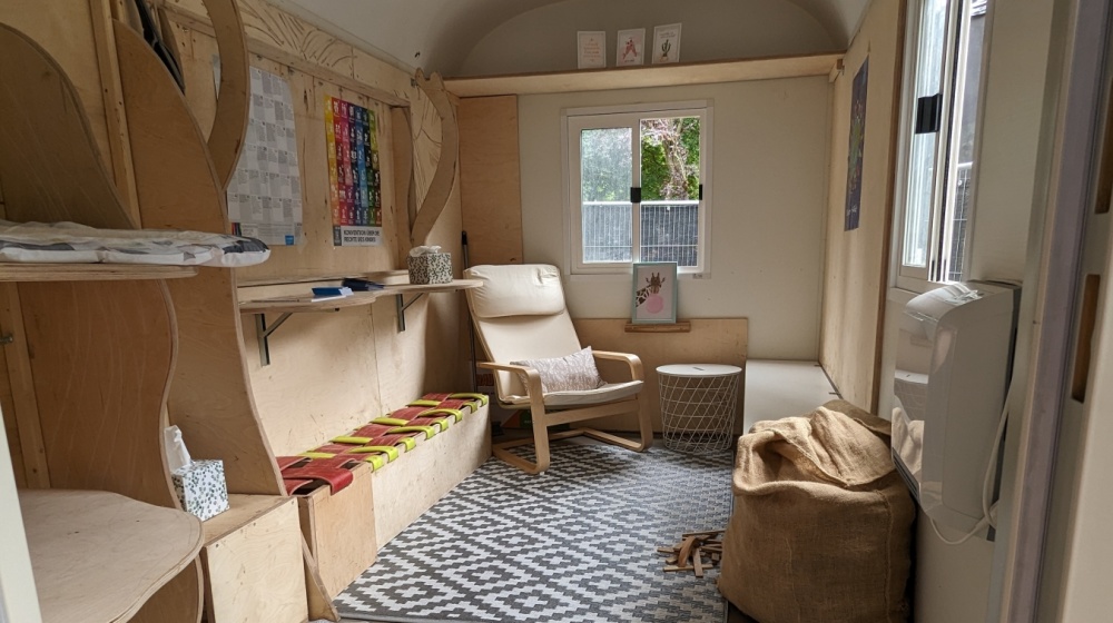 Bauwagen Kinderrechte innen Bauwagen Kinderrechte Innenansicht mit Stuhl, Wickeltisch, Infoplakaten, Fenstern, Deko und Stauraum für Materialien. Alles ist in natürlichen Holzfarben gehalten.