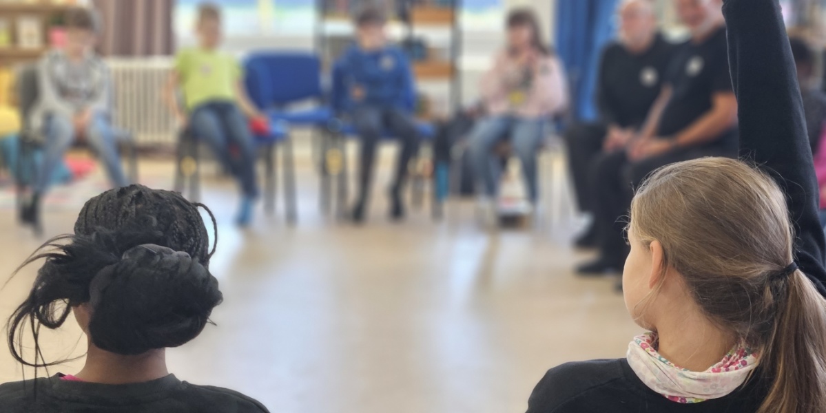 Jung trifft Alt Kinder und Erwachsene sitzen im Stuhlkreis, ein Kind meldet sich