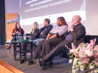 Podium beim Auftakt Demokratie leben 2025 Menschen auf einem Podium vor der Leinwand im Filmhaus Saarbrücken