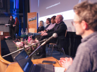 Uwe Albrecht vom Adolf-Bender-Zentrum und das Podium beim Auftakt Demokratie leben ein Mann steht am Laptop und auf der Bühne sitzen Menschen auf dem Podium