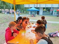 Kinder lernen spielerisch deutsch während des Sprachcamps; sitzen an einer Bank unter einem gelben Zelt