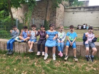 Kinder mit bemalten Gesichtern sitzen auf einer Mauer vor der Bildungswerkstatt