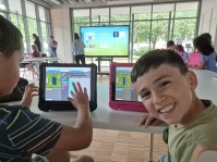 Kinder sitzen zusammen am Tisch mit Tablets; Kind lächelt in die Kamera