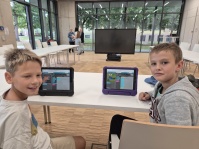Kinder sitzen zusammen am Tisch mit Tablets; Kind lächelt in die Kamera
