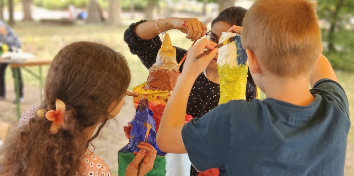 Kunst im Sprachcamp drei Kinder basteln draußen einen bunten Turm