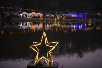 Leuchtende Sterne schwimmen auf dem Weiher und spiegeln sich im Wasser, dahinter Marktstände.