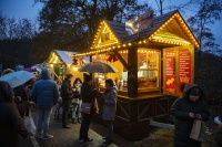 Menschen warten vor einem hell beleuchteten Crêpes- und Waffelstand, einige unter Regenschirmen.
