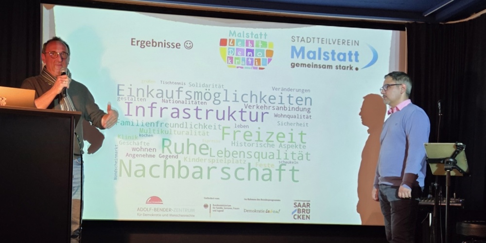 Der Verein MAGS präsentiert sein Projekt Ein Mann mit Mikrofon vor einer Leinwand
