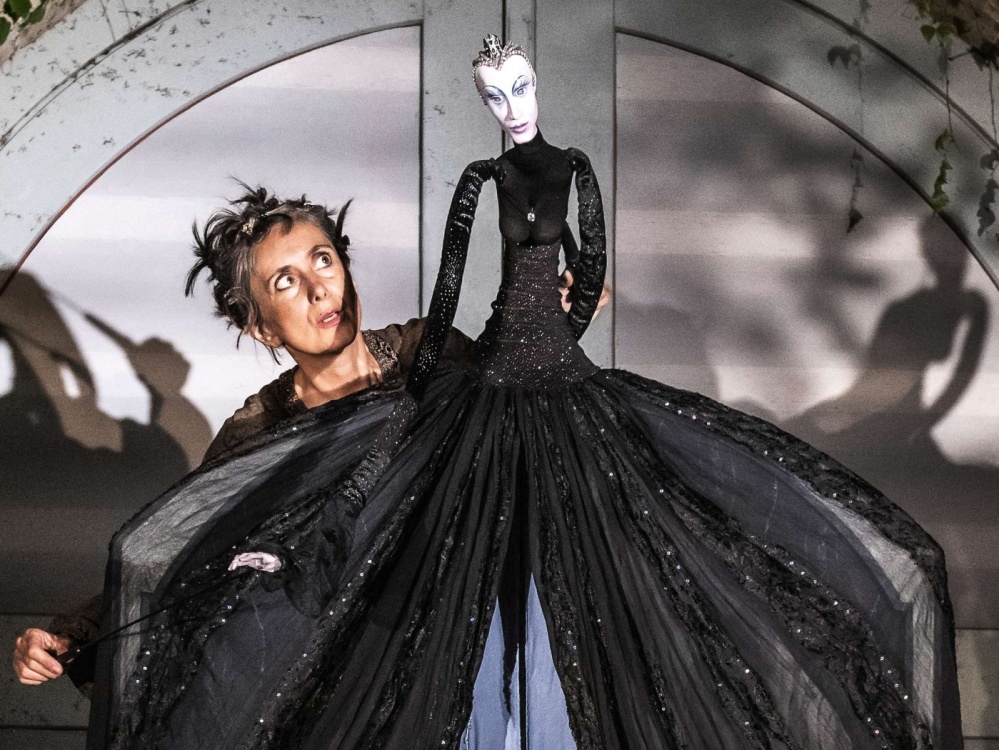 Szene aus "Die Zauberflöte" Eine Frau hält die in einem schwarzen Kleid gehüllte Figur der Königin der Nacht.