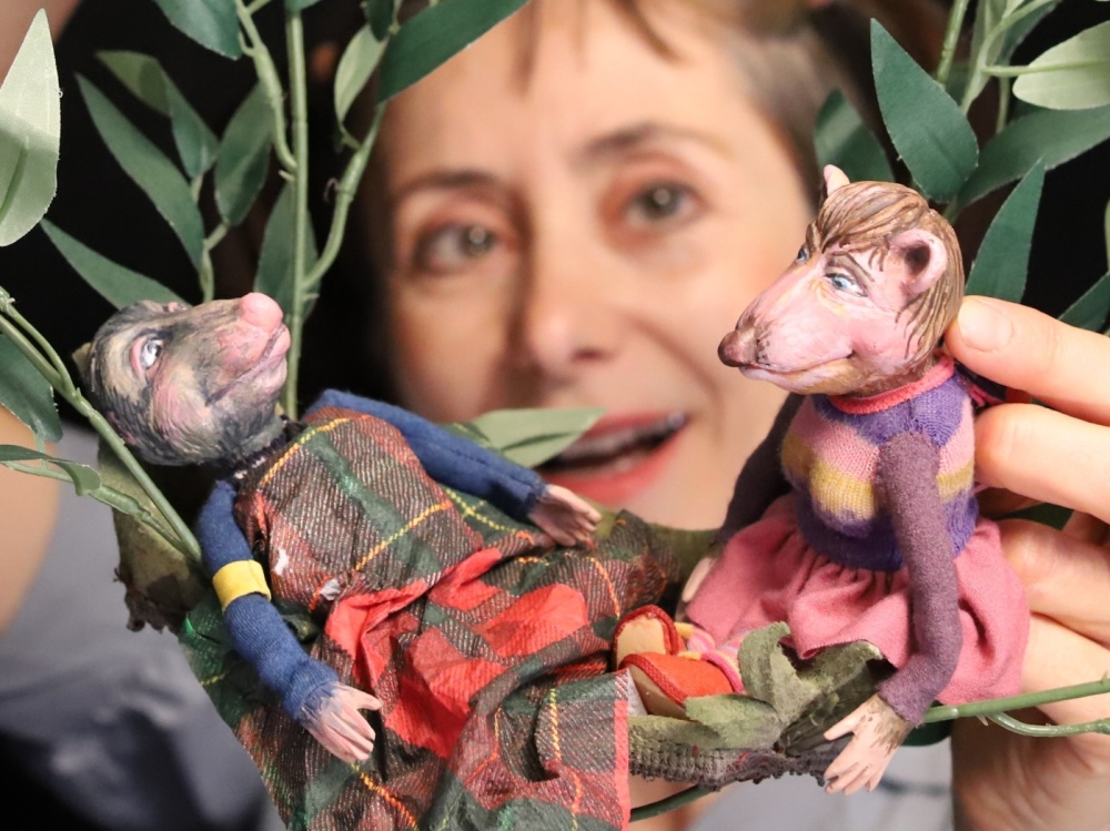 Szene aus "Der Wind in den Weiden" Eine Frau hält Zweige in den Händen, in denen zwei Spielfiguren sitzen.
