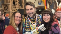 Ein Mann und zwei Frauen halten einen Schlüssel mit der Aufschrift "2026" in der Hand