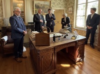 Mehrere Personen stehen in einem edlen Büro mit einer Einrichtung aus den 50ger Jahren.