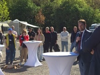 Eine Gruppe von Menschen steht im Halbkreis um einen Stehtisch an dem ein Mann mit Mikrofon spricht