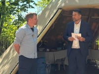 Zwei Männer stehen vor einem Tipi unter einem Baum