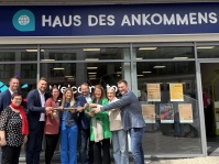 Neun Personen halten einen großen Symbolschlüssel vor einem Haus